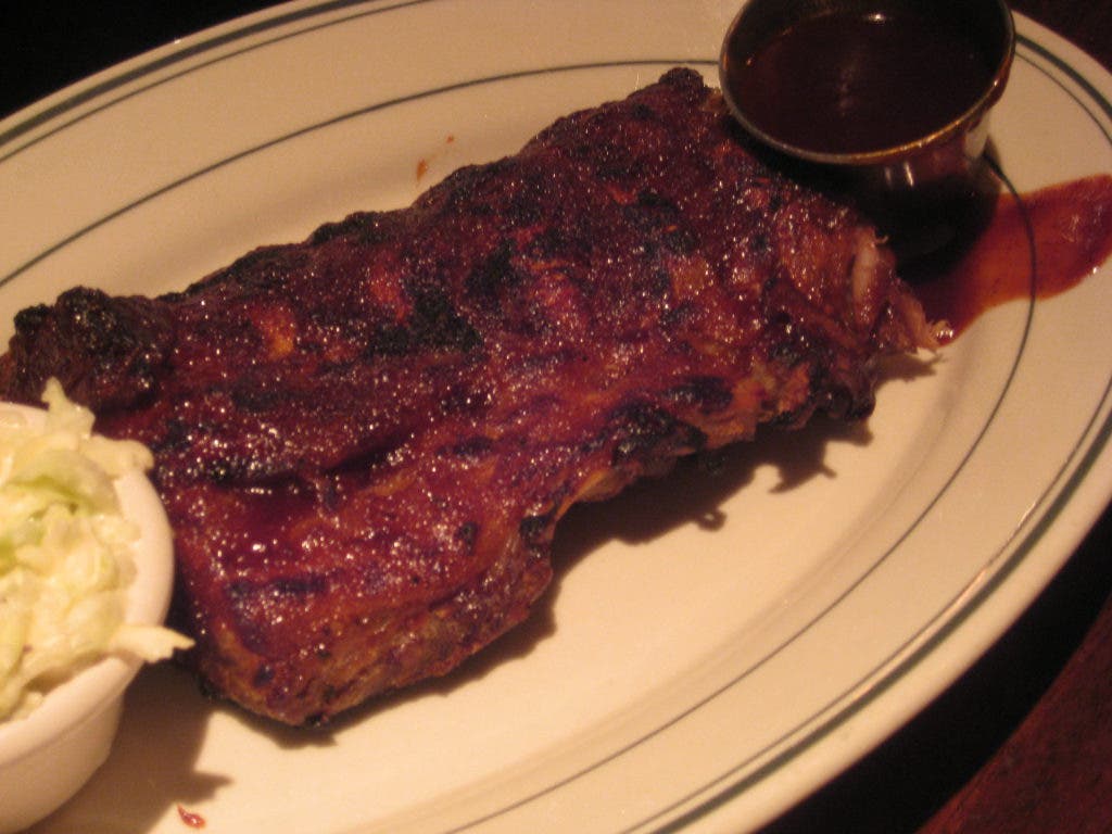 A plate of ribs with coleslaw and BBQ sauce.