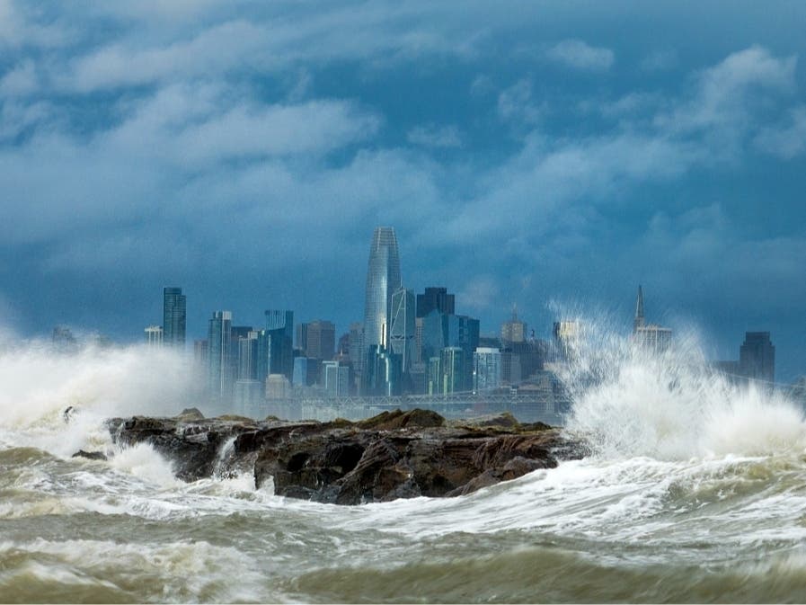Waves crash over a breakwater in Alameda, Calif., with the San Francisco skyline in the background on Sunday, Feb. 4, 2024. High winds and heavy rainfall are impacting the region. 