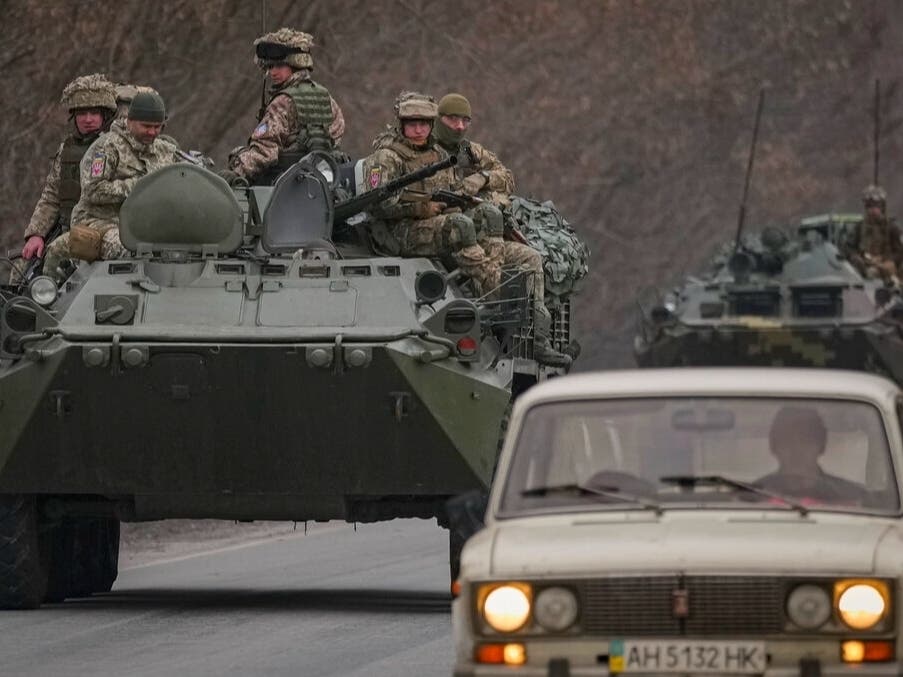 Ukrainian servicemen sit atop armored personnel carriers driving on a road in the Donetsk region, eastern Ukraine, Thursday, Feb. 24, 2022.