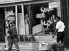 In this July 15, 1967, file photo, a National Guard officer passes the smashed window of a flower shop in Newark, N.J.