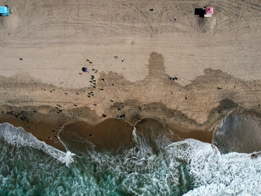 This Monday, Oct. 11, 2021, aerial file photo taken with a drone, shows beachgoers as workers in protective suits continue to clean the contaminated beach in Huntington Beach, Calif. 
