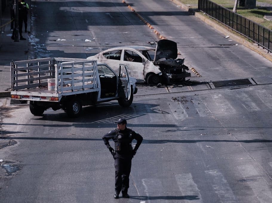 A police officer stands guard by a charred vehicle after it was set on fire, on a road in Guadalajara, Jalisco state, Mexico, Sunday, Feb. 22, 2026, after the death of the leader of the Jalisco New Generation Cartel.