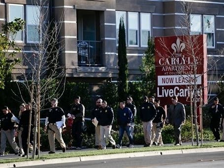 Federal agents walk along the apartment complex, Tuesday, March 3, 2015, in Irvine, Calif., to conduct a crackdown on alleged maternity tourism rings. 