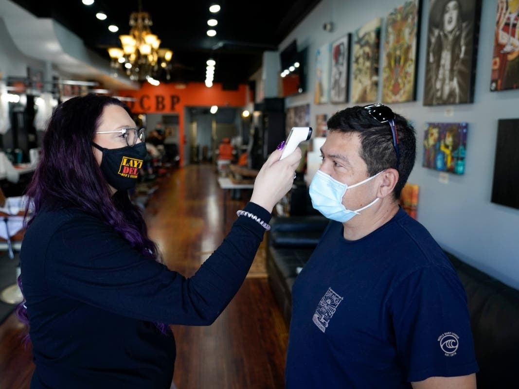Rudy Pulido has his temperature checked by Melissa Acosta before he had his hair cut at Orange County Barbers Parlor in July, Huntington Beach, Calif. 