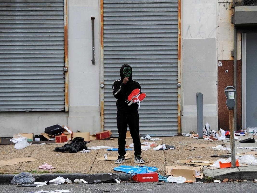 A man stands holds merchandise outside of a damaged store after protest, Tuesday, Oct. 27, 2020, in Philadelphia over the death of Walter Wallace, a Black man who was killed by police in Philadelphia.