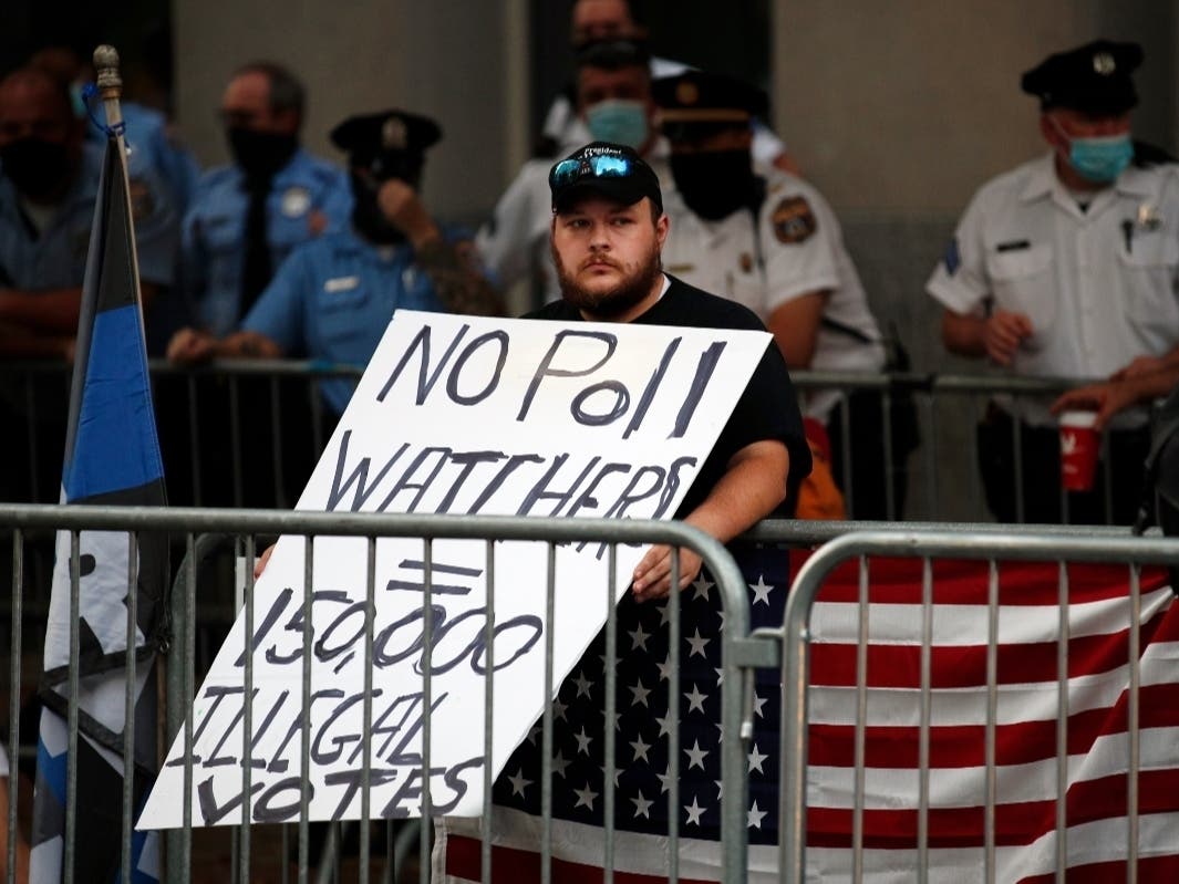 A supporter of President Donald Trump holds a protest sign as police stand guard behind, outside the Pennsylvania Convention Center in Philadelphia, Sunday, Nov. 8, 2020, a day after the 2020 election was called for Democrat Joe Biden.(AP Photo/Rebecca Bl