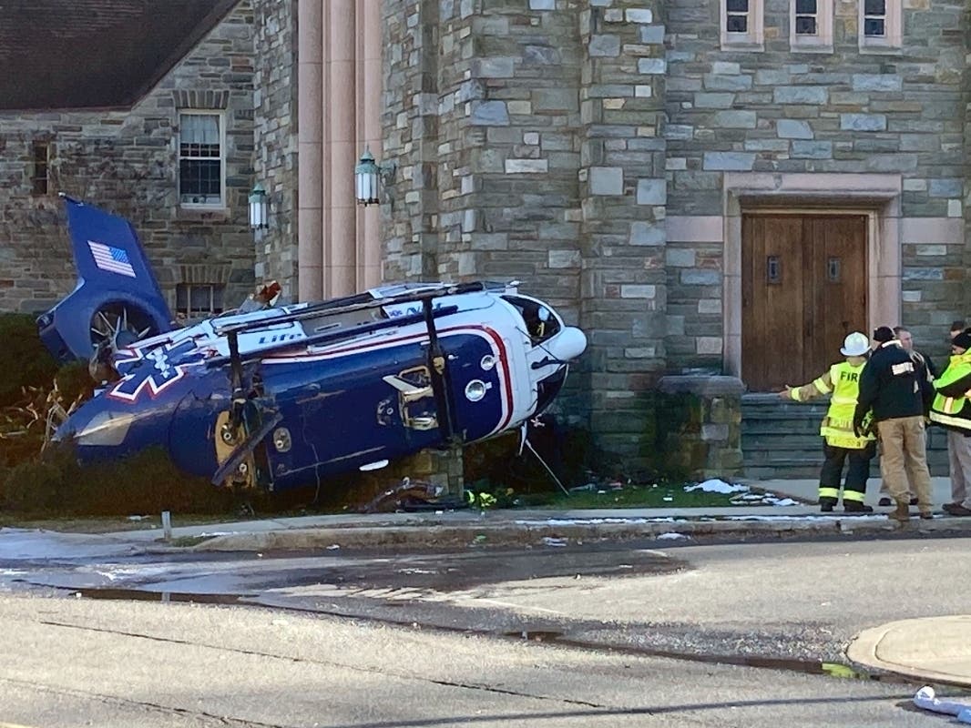 Firefighters from Upper Darby, Pa, stand near a medical helicopter that crashed next to a church in a residential area of suburban Philadelphia, Tuesday, Jan. 11, 2022, with four people on board including an infant. All are expected to survive.