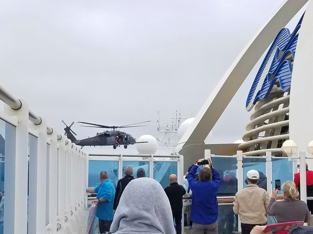 In this photo provided by Michele Smith, passengers look on as a National Guard helicopter hovers above the Grand Princess cruise ship Thursday, March 5, 2020, off the California coast. 
