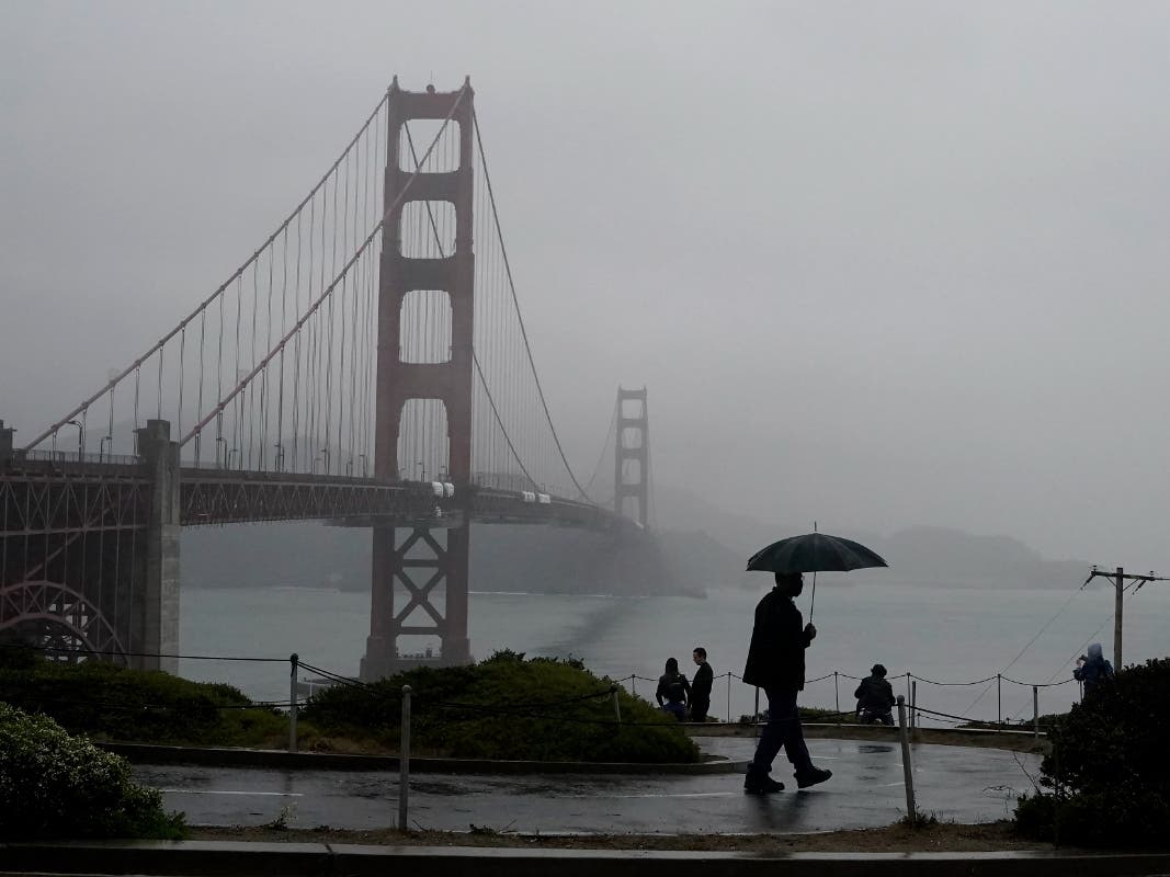 A pedestrian carries an umbrella while walking on a path in front of the Golden Gate Bridge in San Francisco.