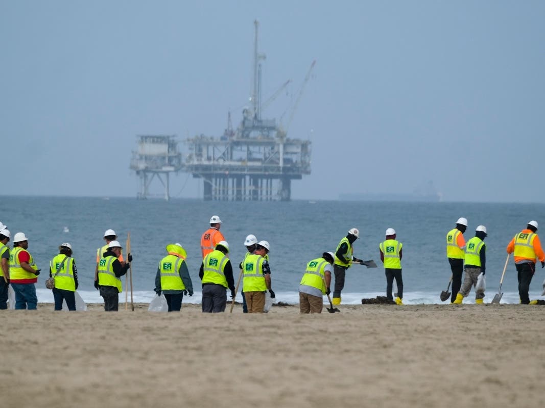 Workers in protective suits continue to clean the contaminated beach with a platform in the background in Huntington Beach, Calif., on Oct. 11, 2021.