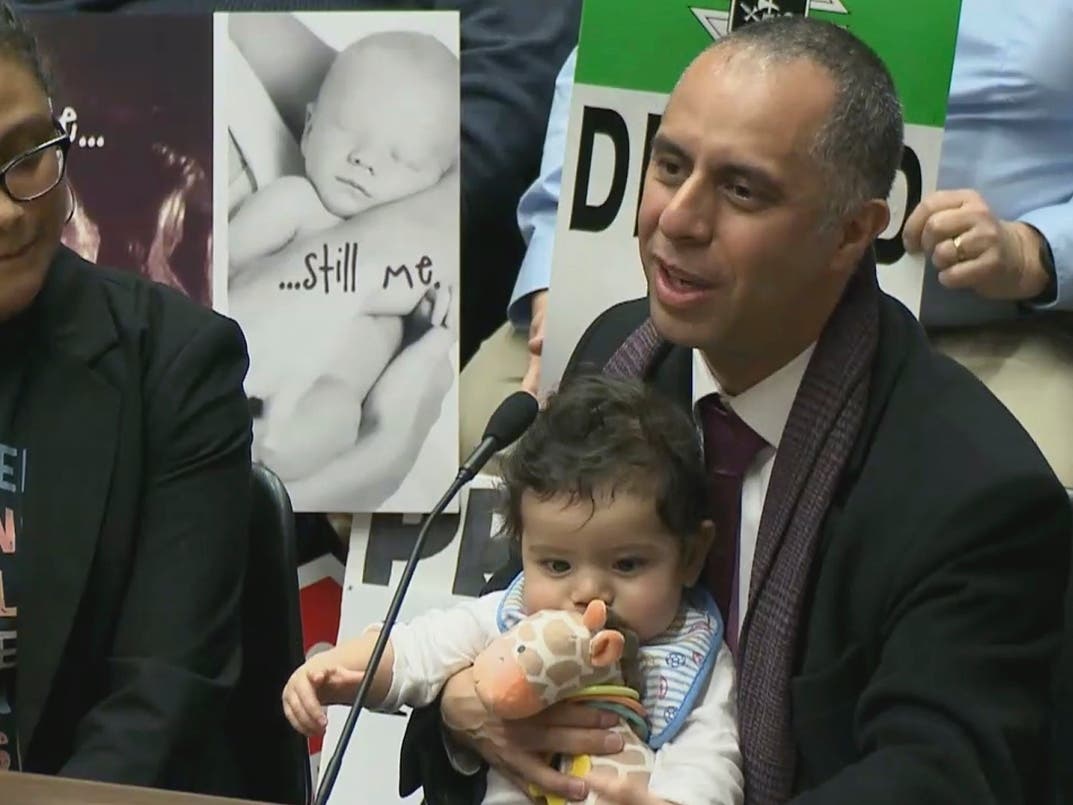 Mayor Jorge Elorza holds his son Omar as he testifies before the House Judiciary Committee at the Statehouse in Providence, R.I.