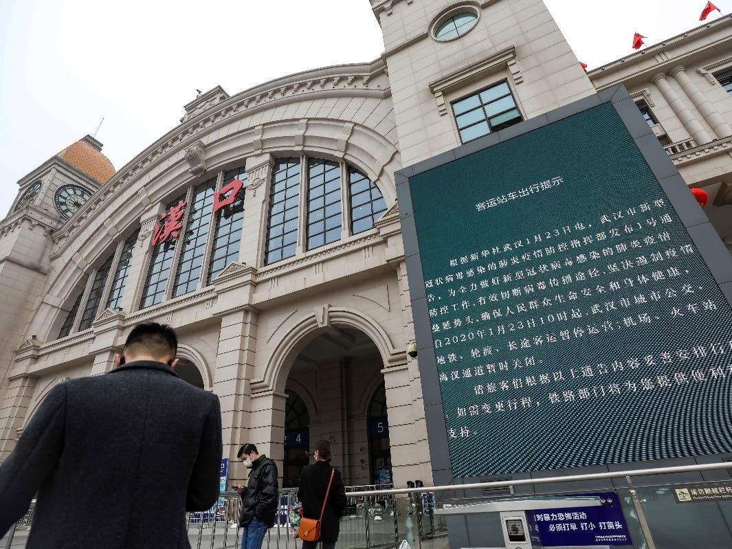People walk past a billboard Thursday announcing the closure of the Hankou Railway Station in Wuhan in central China's Hubei Province.