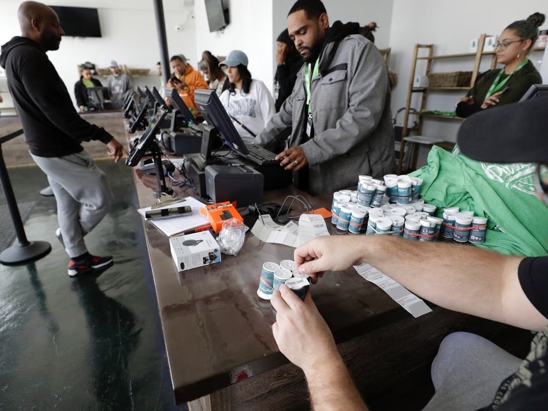 Mike Whittaker, of Quincy, (below right) director of operations at Pure Oasis recreational marijuana shop, applies bar codes to containers of cannabis flowers as workers rehearse using registers in the store.