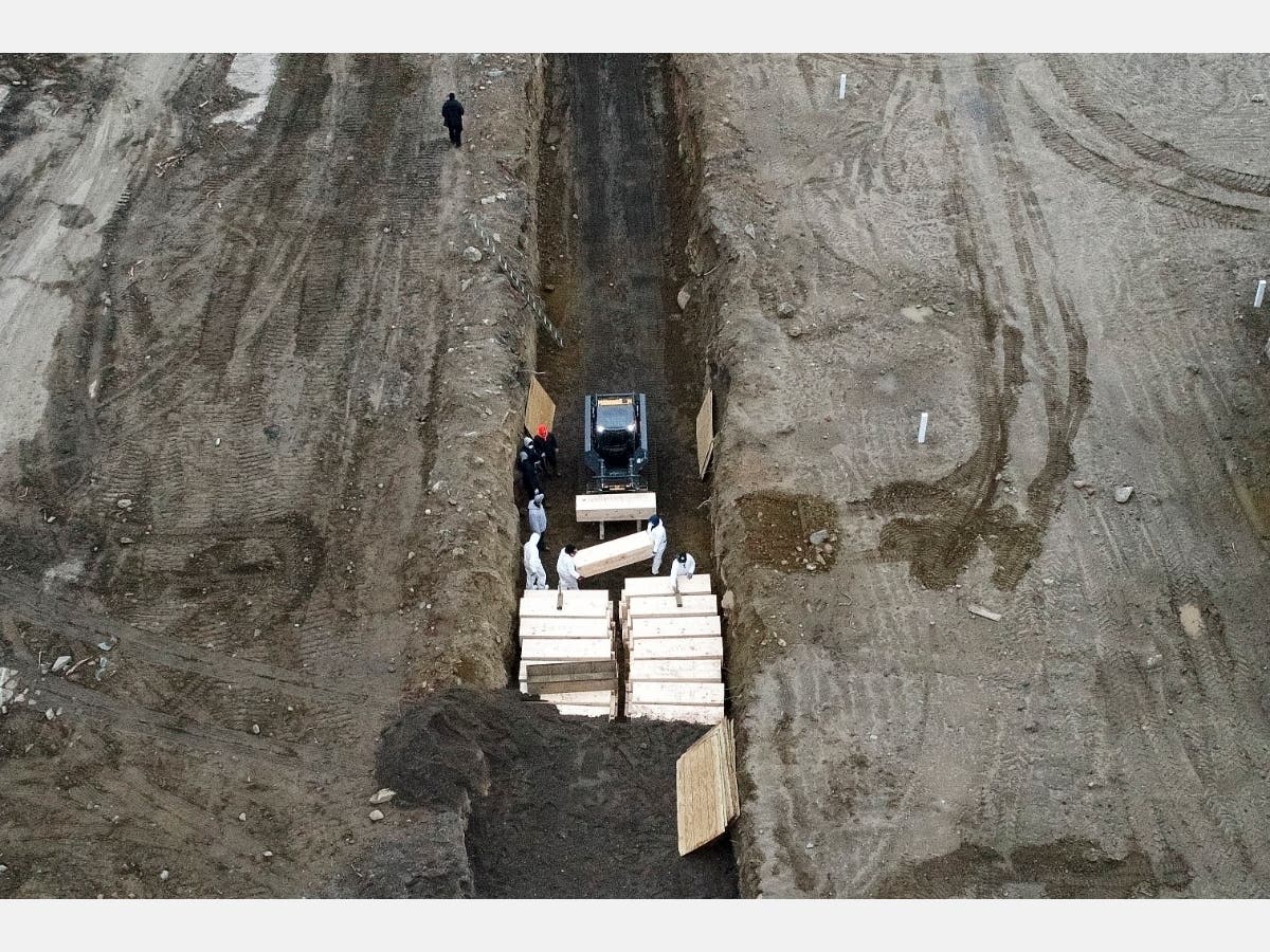 Workers wearing personal protective equipment bury bodies in a trench on Hart Island, Thursday, April 9, 2020.