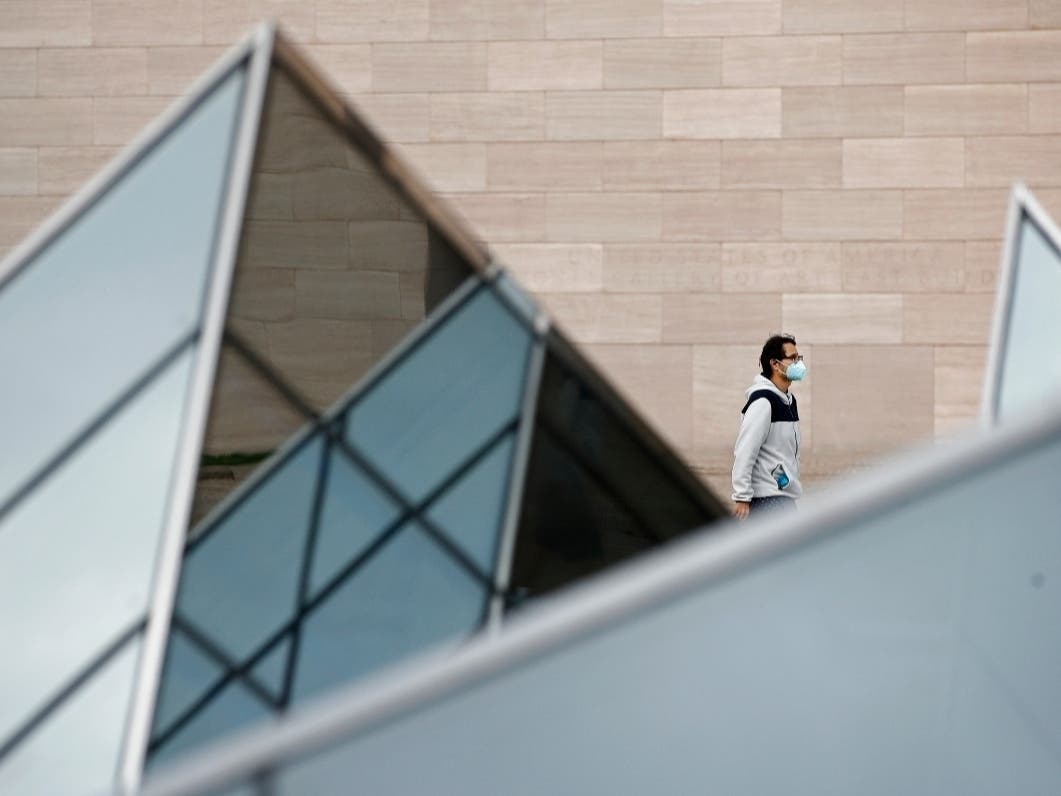 Whether Americans wear a face mask, as this man walking past an art installation outside the National Gallery of Art in Washington, D.C., did Wednesday, may depend on their political persuasions.