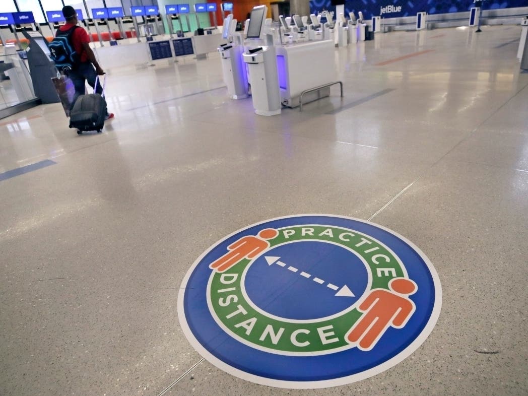 A traveler passes a sign recommending practicing social distancing at Logan Airport in Boston.