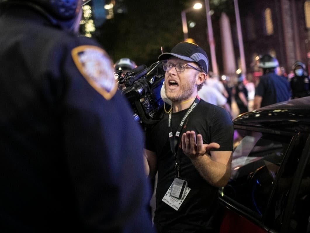 Associated Press videojournalist Robert Bumsted reminds a police officer that the press are considered “essential workers" and are allowed to be on the streets despite a curfew.