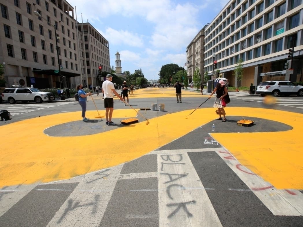 City workers and activists paint the words Black Lives Matter in enormous bright yellow letters on the street leading to the White House.