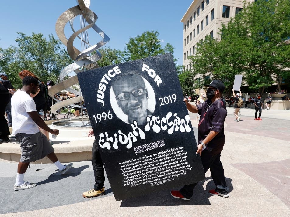 In this June 27, 2020, file photo, demonstrators carry a giant placard during a rally and march over the death of 23-year-old Elijah McClain outside the police department in Aurora.