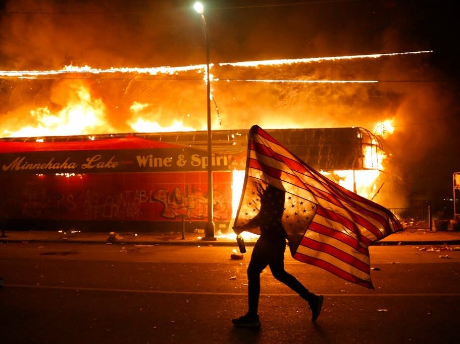 A demonstrator carries a American flag upside down, a sign of distress, next to a burning building in Minneapolis. Protests over the death of George Floyd, a Black man who died in police custody, are among the crises besieging President Donald Trump.