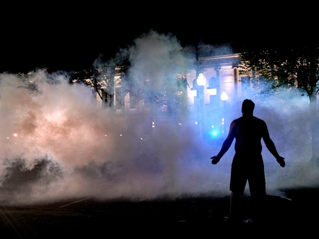 A protester attempts to continue standing through a cloud of tear gas fired by police outside the Kenosha County Courthouse, late Monday, Aug. 24, 2020, in Kenosha, Wis.