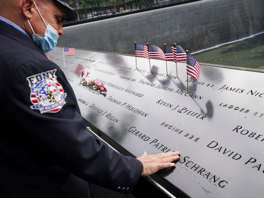 A mourner brushes water with his fingers over the name cut-outs of the deceased at the National September 11 Memorial and Museum, Friday, Sept. 11, 2020, in New York.