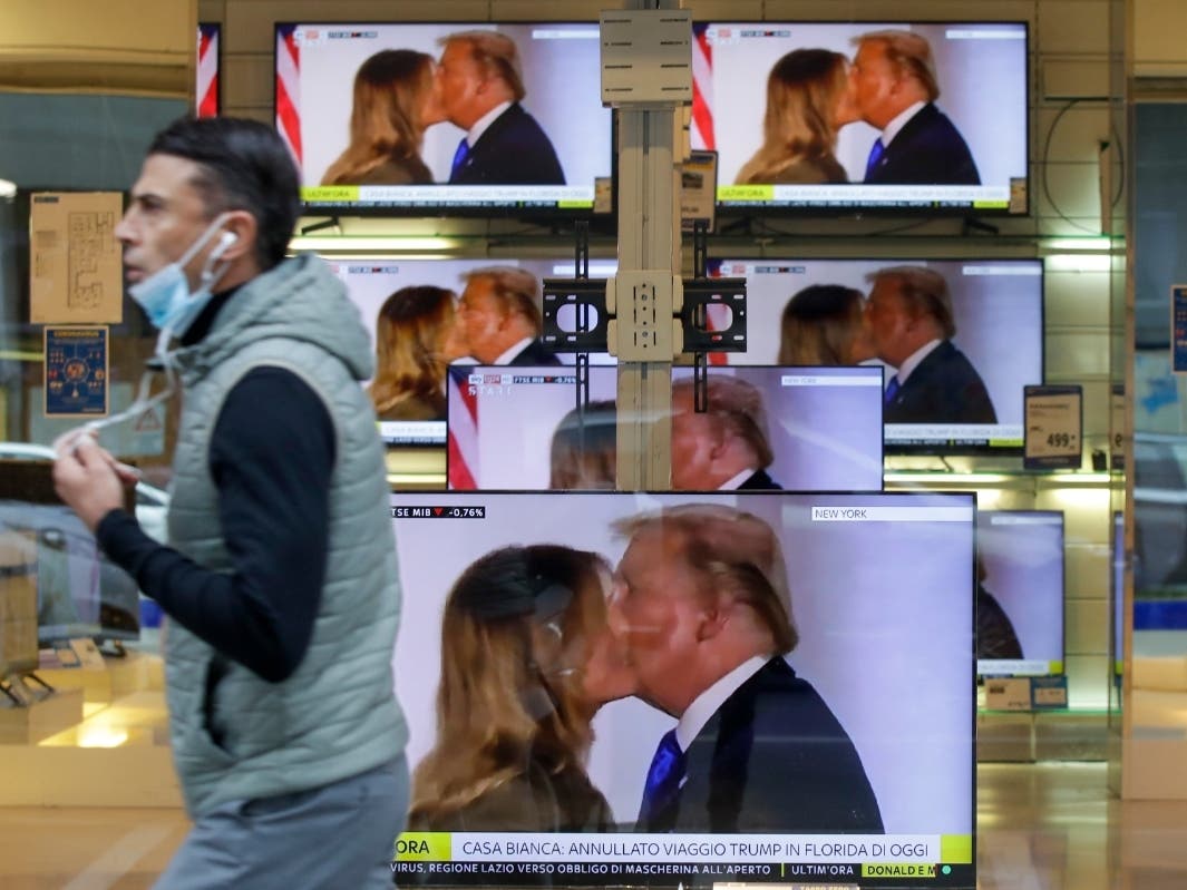 A man wearing a face mask walks by the window of a shop with TV screens showing an image of U.S. President Donald Trump during a news program, in Milan, Friday after Trump announced he and the first lady tested positive for the coronavirus.