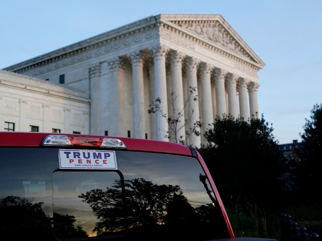 The U.S. Supreme Court looms large in the background as a pickup truck with a Trump-Pence sticker in the back window drives past.