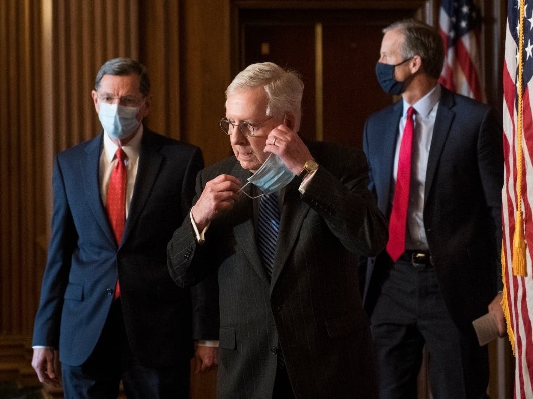 Senate Majority Leader Mitch McConnell of KY., removes his face mask as he arrives with Sen. John Barrasso, R-Wyo., left, and John Thune, R-S.D., right, for a news conference with other Senate Republicans on Capitol Hill.