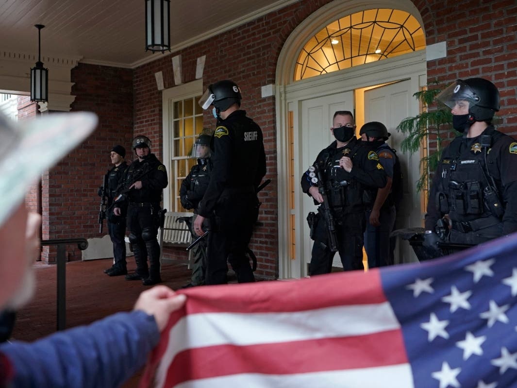  In this Jan. 6, 2021 file photo, protesters square off with law enforcement officers on the front porch of the Governor's Mansion after a group of people got through a perimeter fence at the Capitol in Olympia