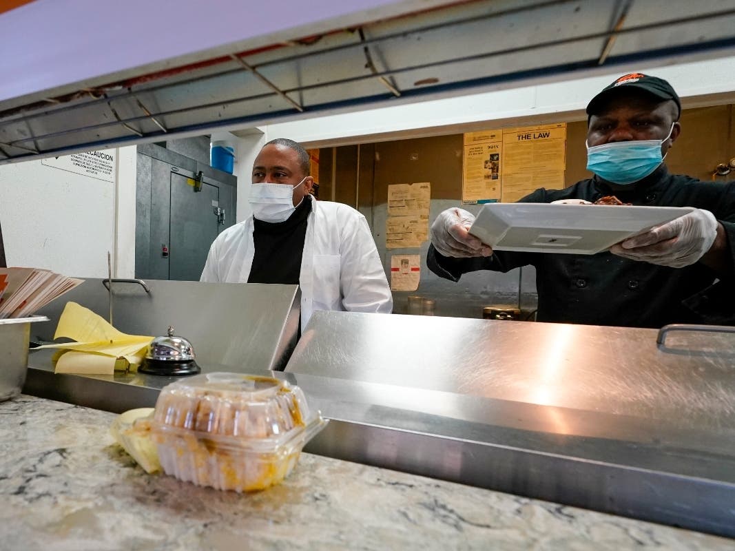 Andrew Walcott, left, owner of Fusion East Caribbean & Soul Food restaurant, monitors the take out orders as his chef Andrew Jackson places an order on the counter at the restaurant in East New York neighborhood of Brooklyn.