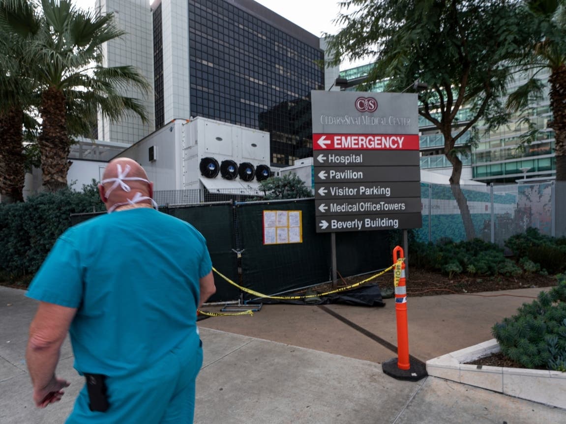 A medical worker walks past a refrigerated trailer parked outside the Cedars-Sinai Medical Center in Los Angeles.