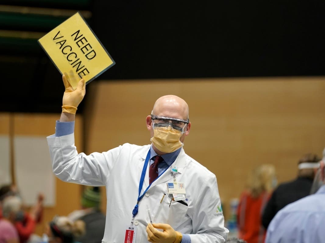 Dr. John Corman, the chief clinical officer for Virginia Mason Franciscan Health, holds a sign that reads "Need Vaccine" to signal workers to bring him more doses of the Pfizer vaccine for COVID-19 in Seattle.