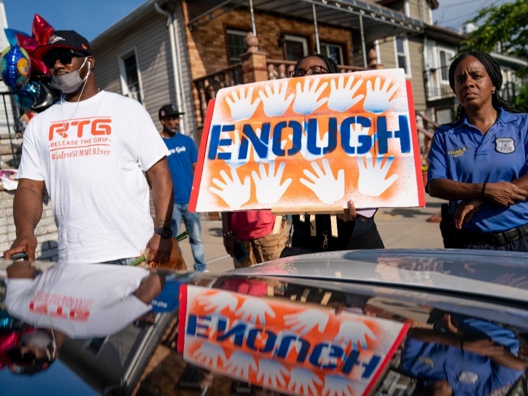 Community members and police attend a vigil beside a makeshift memorial at the scene where 10-year old Justin Wallace was shot and killed the previous Saturday night in the Rockaways.