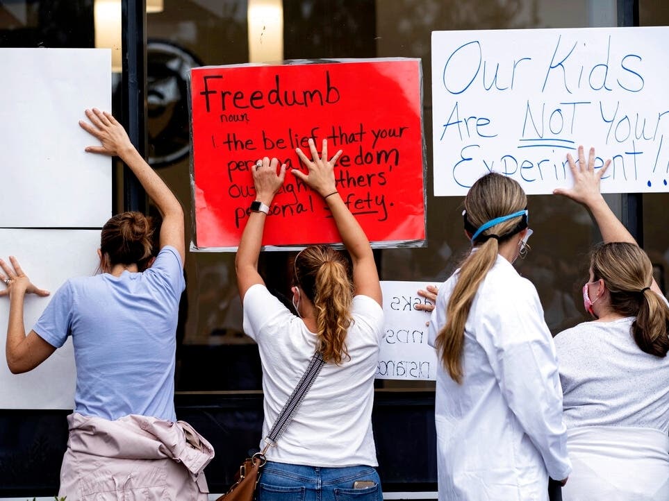 People in favor of a mask mandate for Cobb County schools hold signs against the window to the office during the school board meeting in Marietta, Georgia. 