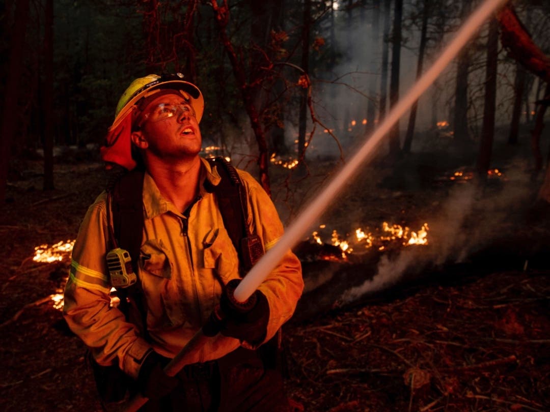 A firefighter hoses down flames from the Dixie Fire in Genesee, Calif., on Saturday, Aug. 21, 2021.