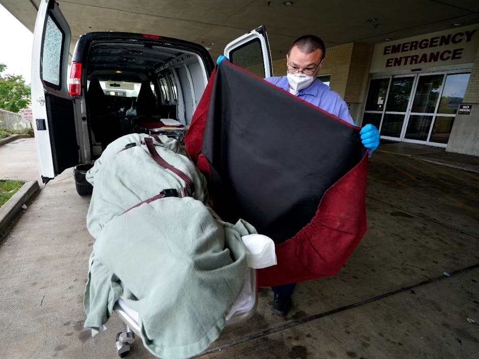 An employee of a local funeral home covers the body of a COVID-19 patient patient as he prepares to take it away from a loading dock at the Willis-Knighton Medical Center in Shreveport, Louisiana.