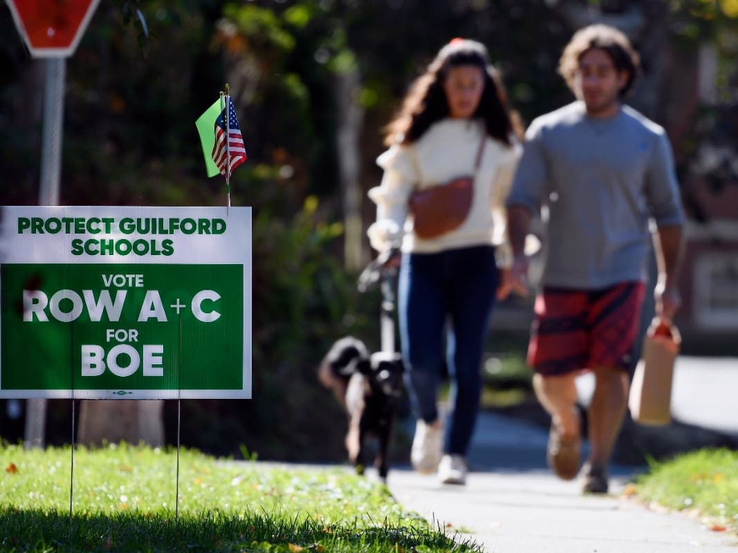 People walk near one of many signs around town centered around the upcoming Nov. 2 election and equity initiatives in schools in Guilford, Connecticut, on Tuesday, Oct. 19.