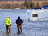 Two men stand in the flooded Skagit River and look across at an RV, Monday, Nov. 15, 2021, in Sedro-Woolley, Wash.