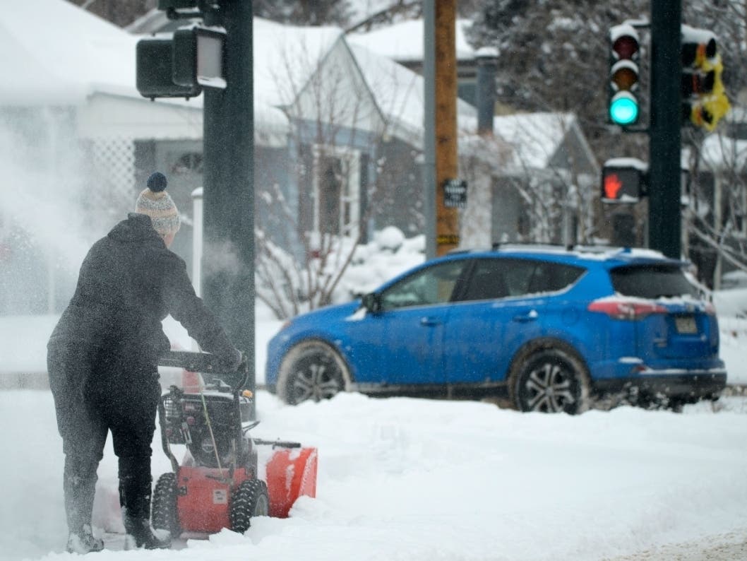 ​A woman uses a snowblower to clear a walkway as a motorist struggles to turn on a snow-packed Denver street Wednesday. The storm was expected on to the Midwest, which is bracing for heavy snowfall and icy conditions in the days ahead.