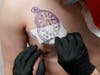 Tattoo artist Tom Begley of the "Electric Tattoo Parlor" in Carpentersville, Ill., pulls back a stencil of a tattoo for Jaime Marinez to cover a bullet hole scar that depicts the date and time of Marinez's father's death.