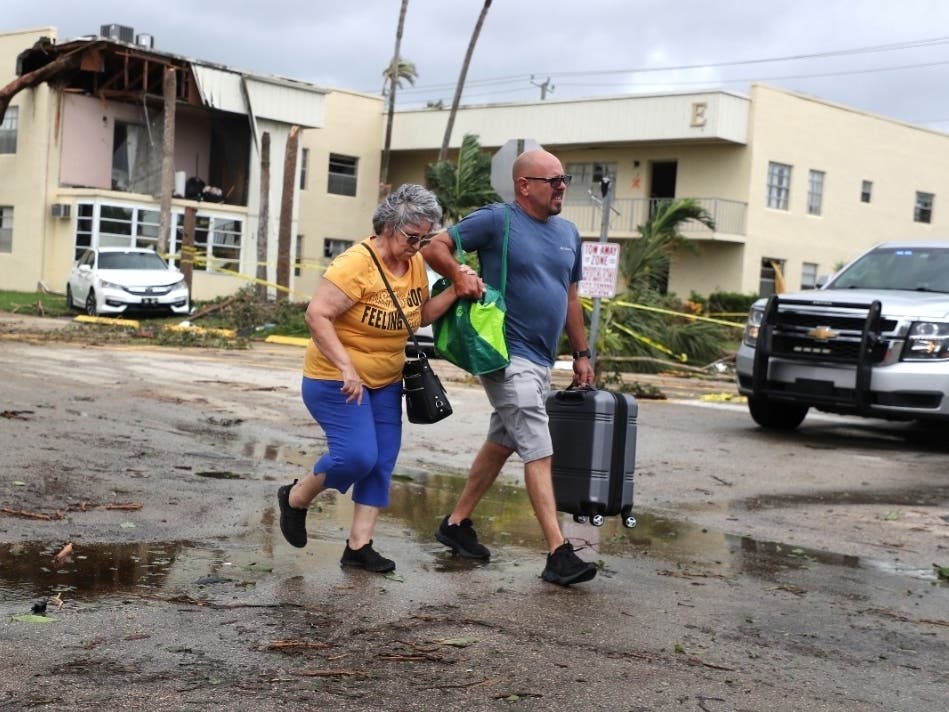 King Point resident Maria Esturilho is escorted by her son Tony Esturilho as they leave behind the damage from an apparent overnight tornado spawned from Hurricane Ian at Kings Point 55+ community in Delray Beach, Florida, on Wednesday.