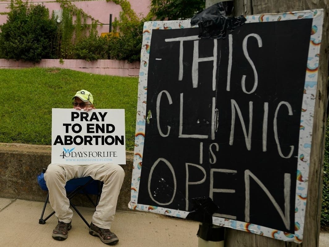 An abortion foe is pictured July 6 behind a sign advising the Jackson Women's Health Organization clinic remained open. It has since closed, a response to the Supreme Court's Dobbs v. Jackson ruling in June ending 50 years of federal abortion protections.
