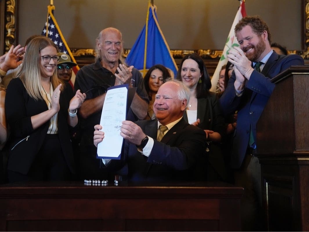 Minnesota Gov. Tim Walz, middle, holds the bill signed to legalize recreational marijuana for people over the age of 21, making Minnesota the 23rd state to do so, Tuesday, May 30, 2023, in St. Paul, Minn. Former Gov. Jesse Ventura stands at center.
