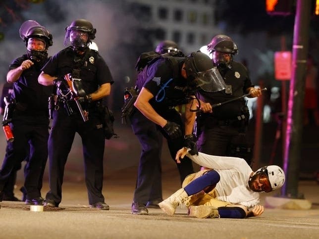  Denver Police Department officers clear a man who fell to the street after they used tear gas and rubber bullets to disperse a protest outside the state Capitol over the death of George Floyd, a man who died in police custody in Minneapolis.