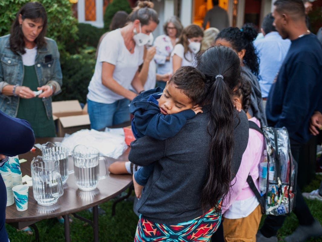 A woman, part of a group of immigrants that arrived on chartered planes to Martha's Vineyard, holds a child as they are fed outside St. Andrews Episcopal Church, Wednesday. 
