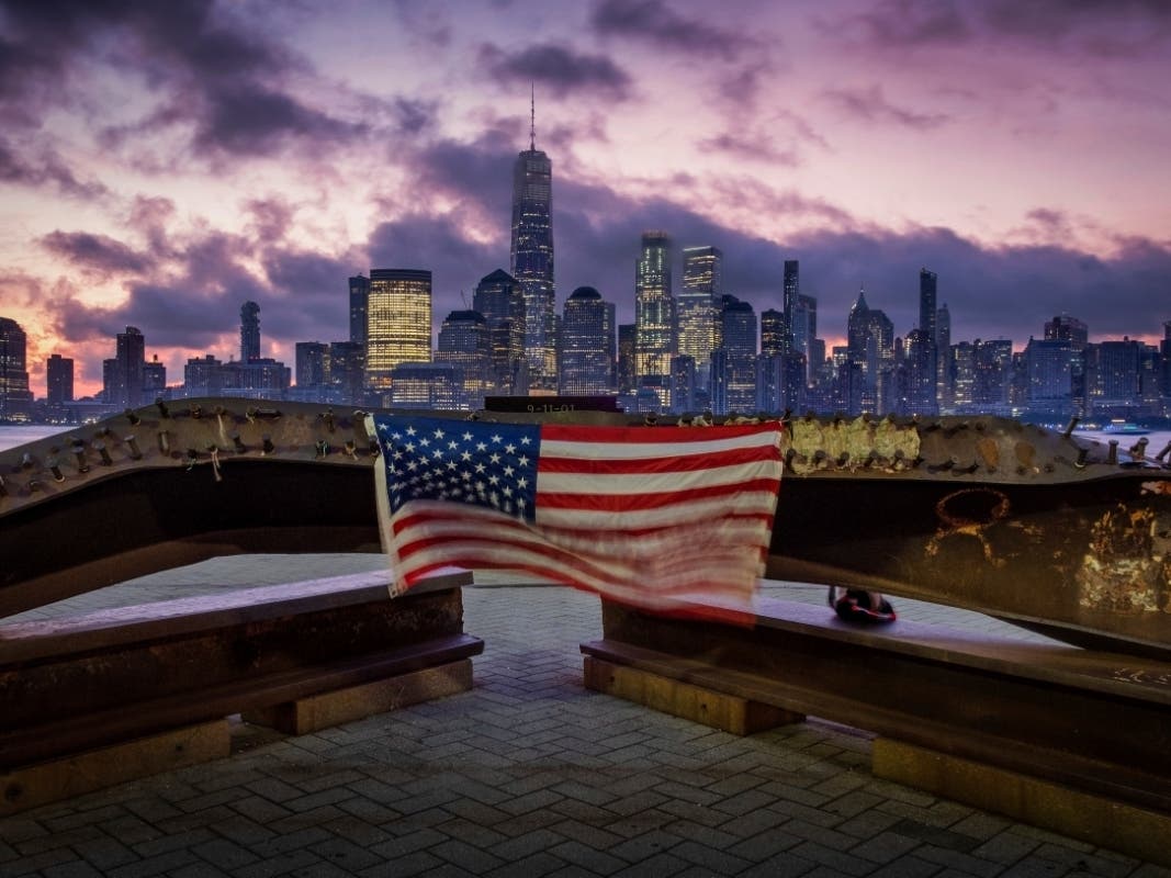A U.S. flag hanging from a steel girder, damaged in the Sept. 11, 2001 attacks on the World Trade Center, blows in the breeze at a memorial in Jersey City, N.J., Sept. 11, 2019 as the sun rises behind One World Trade Center building and the re-developed a