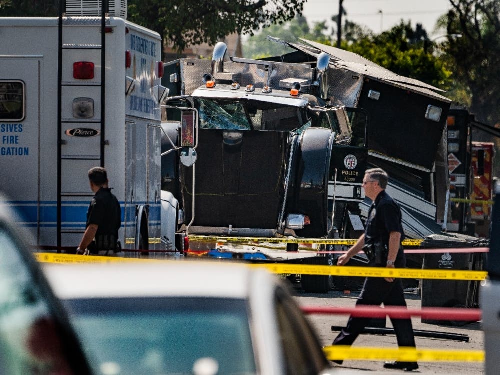 Police officers walk past the remains of an armored Los Angeles Police Department tractor-trailer Thursday morning July 1, 2021, after illegal fireworks seized at a South Los Angeles home exploded Wednesday evening, in South Los Angeles.