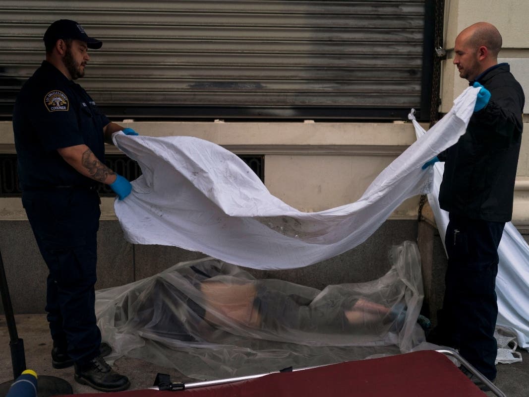 Forensic assistant Laurentiu Bigu, left, and investigator Ryan Parraz from the Los Angeles County coroner's office cover the body of a homeless man found dead on a sidewalk in LA April 18, 2022. The 60-year-old died from the effects of methamphetamine.
