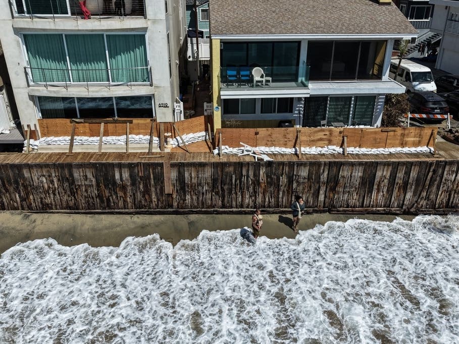 Two people walk along the beach as sandbags and temporary wooden barriers protect homes in preparation for the upcoming storm season in Long Beach, Calif., Wednesday, Sept. 23, 2026. 